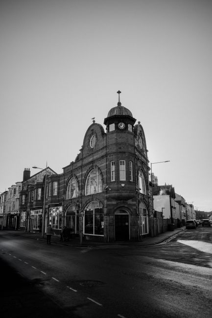 There is no image of flowers or floral arrangements; the photo depicts a historic, multi-story building with a prominent clock tower and a cross on top, situated on a street corner. The building featu